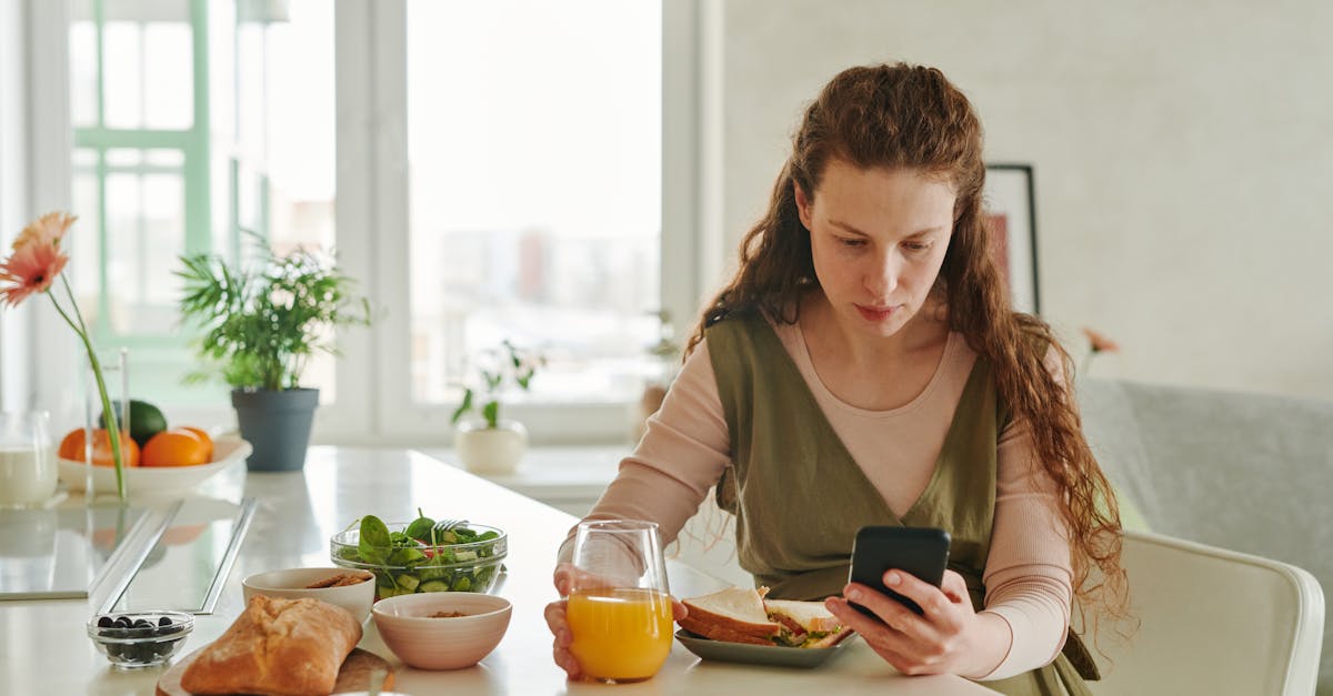 Pregnant woman at breakfast table browsing on smartphone while having a healthy meal indoors.
